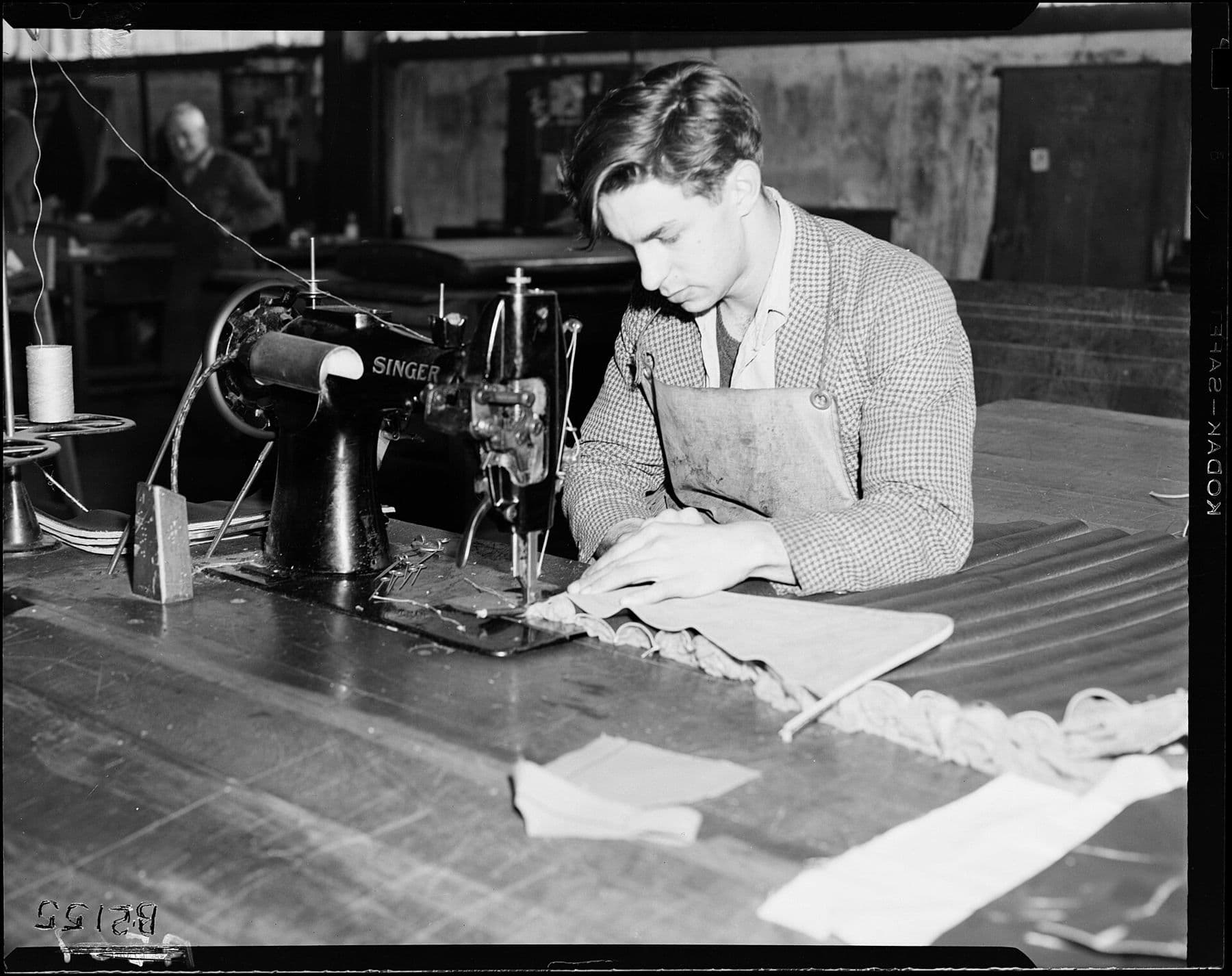 Black and white photograph of an upholsterer working at a sewing machine in a 1953 workshop